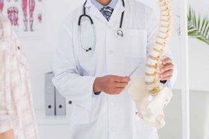 A pregnant person sits upright while a chiropractor gently supports her lower back during an adjustment session.