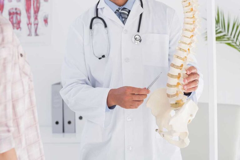 A pregnant person sits upright while a chiropractor gently supports her lower back during an adjustment session.